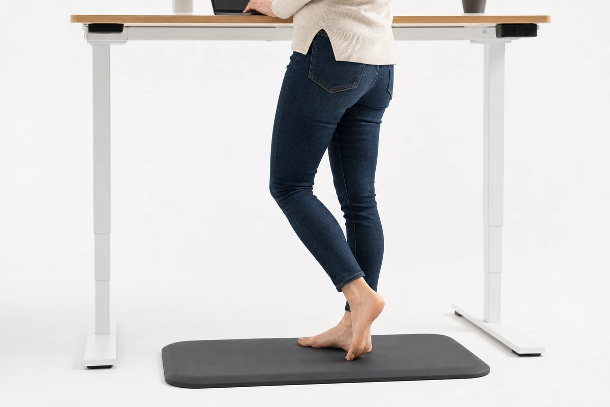 A person at a standing desk shifting their weight on a black anti-fatigue mat